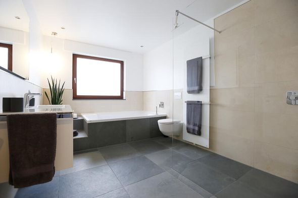 Badezimmer mit dunklen Bodenfliesen und braunen Wandfliesen in Stein-Optik mit großer Dusche und einer Badewanne